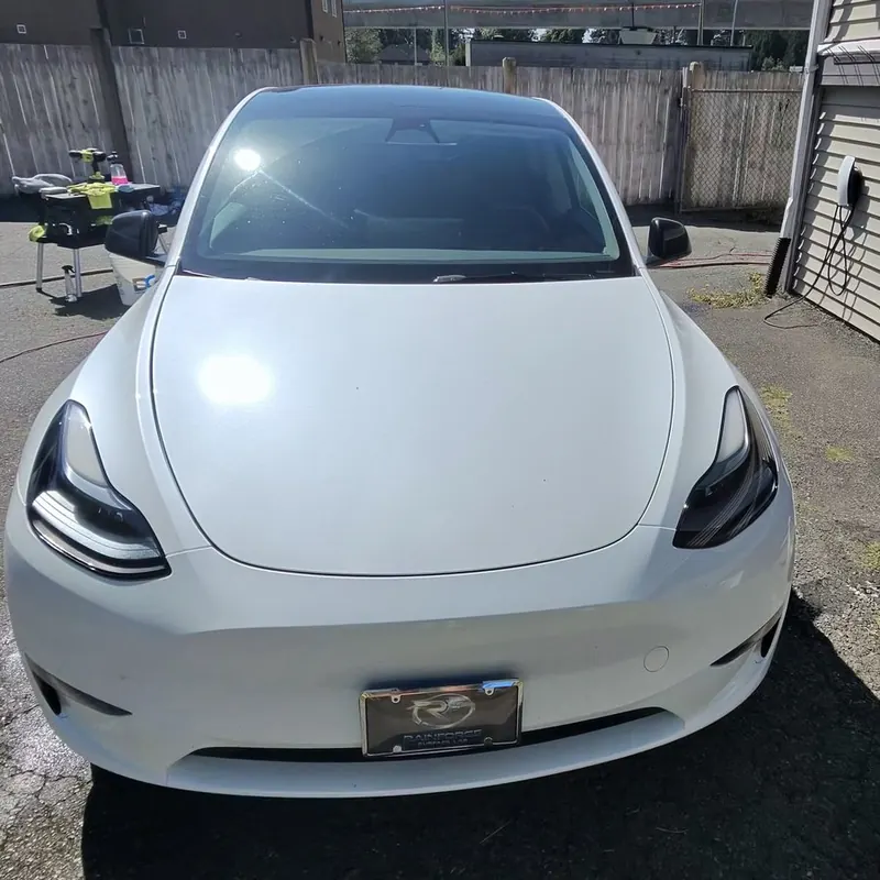 A white electric SUV seen from the front, the Rainforge plate frame on its bumper