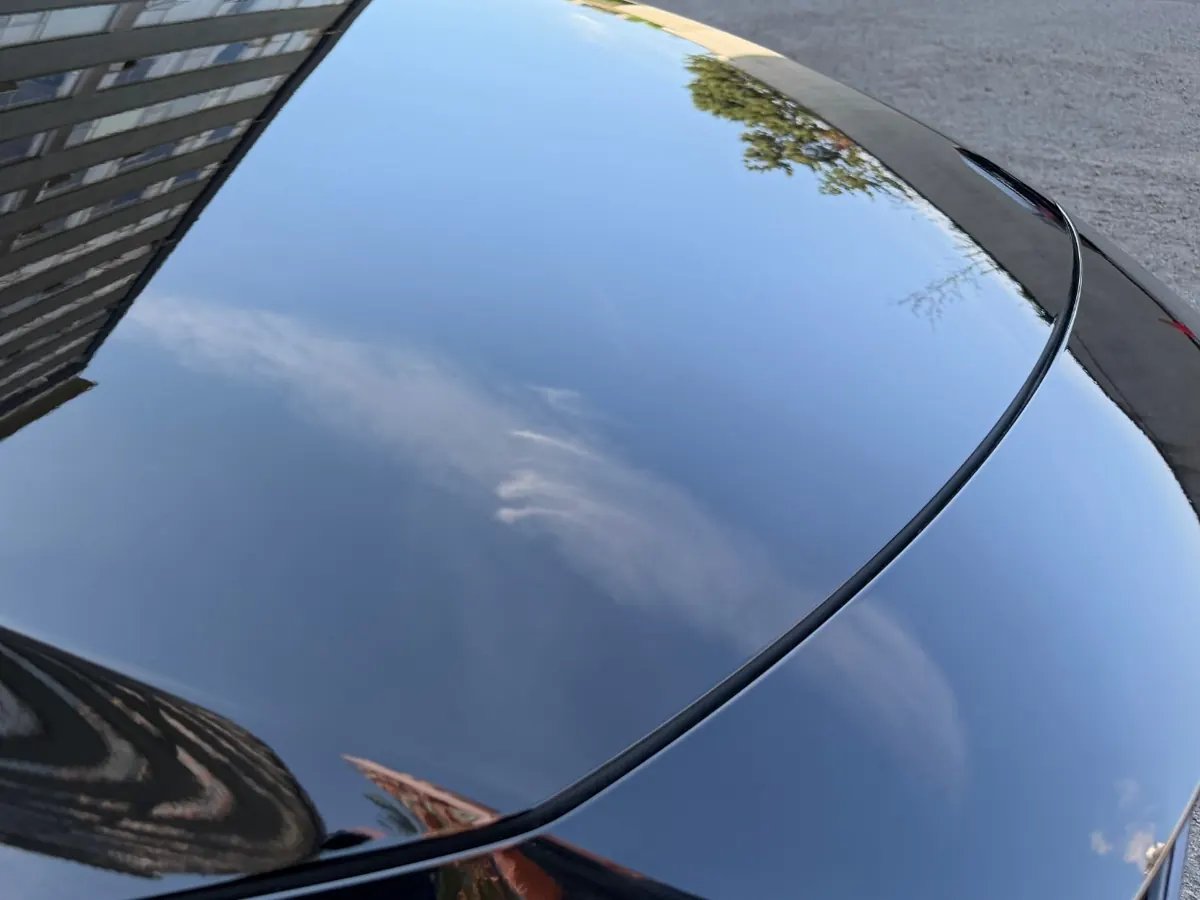 Deep gloss on a black car’s trunk, reflecting the sky