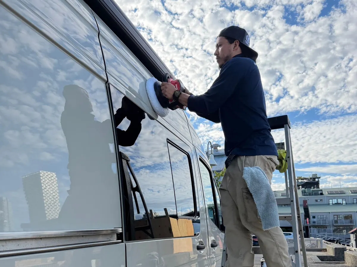 Machine polishing the side of a camper van from a ladder